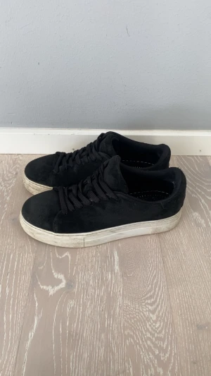 Svarta sneakers i mocka - Svarta sneakers i mocka med tjock vit sula och svarta skosnören. Klassisk låg modell med enkel design som passar till det mesta. Skorna har en stilren look och är perfekta för dig som gillar en clean och tidlös vibe.