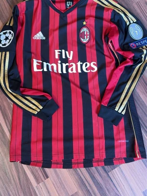AC Milan Hemmatröja 2013/14 ( Robinho ) - Säljer en långärmad AC Milan matchtröja från Adidas med klassiska röda och svarta ränder, guldiga ränder på ärmarna och officiella UEFA Champions League och Respect-patchar. Jätte fin tröja med en av de bästa spelare i världen under denna tid, Robinho. Perfekt för fotbollsfans!