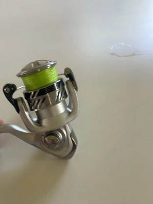 Silverfärgad haspelrulle med gul lina - Säljer en haspelrulle i metall med silverfärgad finish och svart handtag. Rullen är laddad med en gulgrön fiskelina och har en modern design. Perfekt till fiske och passar de flesta spön. Enkel att använda och smidig att ta med sig. Finns inte jättemycket lina.