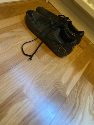 Svarta Nike mercurials  - Säljer ett par svarta fotbollsskor från Nike med klassisk snörning och låg profil. Skorna har en stilren design med vita detaljer och Nike-logga på sidan. Ovandelen är i syntetmaterial som ger bra bollkontroll och passform. Perfekta för dig som vill ha snygga och funktionella skor på planen.