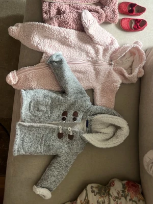 Teddyjacka i grått och vitt med huva - Mysig teddyjacka i grått och vitt med fluffig huva och dekorativa träknappar. Jackan har stora fickor framtill och är fodrad med mjuk teddy på insidan. Perfekt för kyliga dagar och ger en gullig look. En mysig rosa one pose och en mörkrosa flis som två rosa är från hm och den gråa från lupilu och dom röda skorna är från H&M  