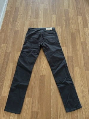 Svarta jeans från J.Lindeberg - Snygga svarta jeans från J.Lindeberg med raka ben och klassisk femficksdesign. Jeansen har en stilren look med diskret logga på en ljus patch bak i midjan. Perfekta för dig som gillar enkel och clean stil.