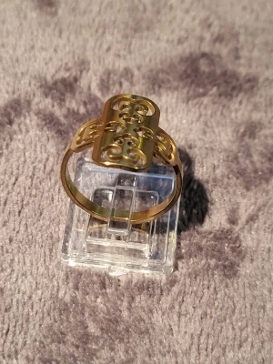 Guldfärgad ring med utskuret mönster - Unik guldfärgad ring med ett rektangulärt, utskuret mönster på ovansidan och sidorna. Ringen har en modern och konstnärlig design med mjuka, böljande former i metallen. Perfekt för dig som gillar statement-smycken och vill sticka ut.