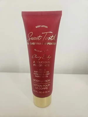 Sabrina Carpenter Cherry Baby Body Lotion - Body lotion i röd tub med guldtext från Sabrina Carpenter, doft Cherry Baby. Innehåller sheasmör, vitamin E, jojobaolja och hyaluronsyra för att återfukta och mjukgöra huden. Doft av körsbär, vallmo, äpple och mörk choklad. 75 ml, endast testad 