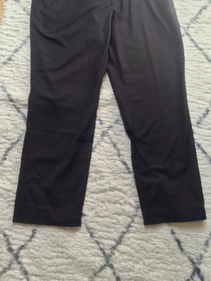 Svarta chinos med rak passform H&M - Säljer ett par svarta chinos med rak passform och klassisk design. Byxorna har diskreta fickor och är tillverkade i ett mjukt, vävt material som ger en clean look. Perfekta för dig som gillar stilrena och enkla plagg.