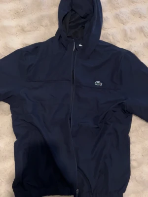Lacoste Tennis Jacka mörkblå - Helt ny mörkblå Lacoste tennis jacka/windbreaker. Den är i helt ny skick med tags fortfarande på. 
