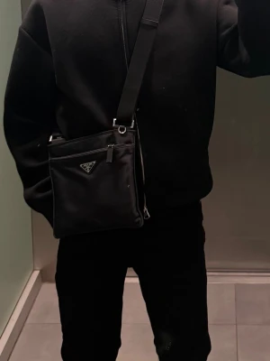 Prada Nylon Crossbody Bag – mycket fint skick - Säljer min Prada crossbody-väska i svart nylon. Väskan är köpt via StockX för cirka 7 000 kr och har gått igenom deras äkthetskontroll/certifiering.  Skicket är mycket bra med endast minimala tecken på användning. Nylonet är fint, remmen är i mycket gott skick och helhetsintrycket är betydligt bättre än de flesta Prada nylonväskor som finns ute på andrahandsmarknaden.  Detaljer:  * Prada nylon crossbody * Svart färg * Justerbar axelrem * Mycket fint skick * Äkthetskontrollerad via StockX 