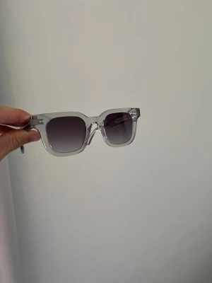 Chimi solglasögon  - Snygga Chimi solglasögon med transparent båge och fyrkantig form. Glasen har en mörkgrå toning som ger en cool vibe. Perfekta för dig som vill ha en stilren och modern accessoar till sommaren. Dem är oanvända och har nypris 1500 kr 