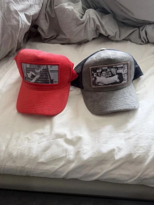 Två kepsar med fototryck - Säljer två kepsar i truckermodell, en röd och en grå med svart nät baktill. Båda har svartvita fototryck framtill som ger en cool och unik look. Perfekt accessoar för att sticka ut i mängden.