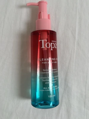 Topz Cleansing Oil 150 ml - Rengöringsolja från Topz i en snygg pumpflaska med rosa, röd och blå färgskiftning. Innehåller solrosfröolja och squalane, passar alla hudtyper och är vegansk. Perfekt för att ta bort smink och rengöra huden på djupet.