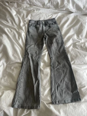 Grå bootcut jeans med utsvängda ben - Säljer ett par gråa bootcut jeans med utsvängda ben och klassisk femficksmodell. Jeansen har normal midja. Perfekta för dig som gillar en retroinspirerad look och vill ha ett par bekväma jeans med snygg passform.