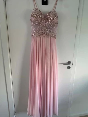 Ljusrosa långklänning med paljetter storlek: L - Elegant ljusrosa långklänning med tunna axelband och vackert dekorerad överdel med paljetter och pärlor. Kjolen är mjukt fallande och ger en romantisk look. Perfekt för bal eller festliga tillfällen. Klänningen behöver kemtvättas innan användning då ev fläck förekommer.