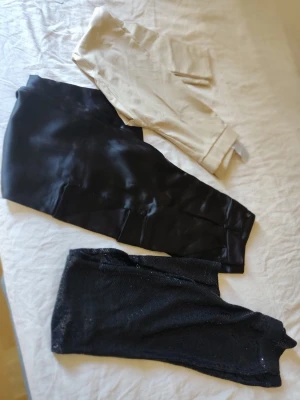 Tre olika byxor i svart och beige - Säljer ett set med tre byxor: ett par beige chinos, ett par svarta cargopants med fickor och ett par svarta leggings med glittrig finish. Perfekt för dig som vill variera din stil och ha både klassiskt och trendigt i garderoben.