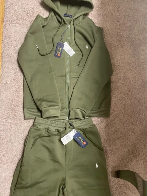 Olivgröna mjukisbyxor Polo Ralph Lauren - Snygga olivgröna mjukisbyxor från Polo Ralph Lauren med dragsko i midjan och klassisk vit logga broderad på benet. Tillverkade i mjukt bomullsmaterial för maximal komfort. Perfekta för chill dagar eller när du vill ha en avslappnad stil.