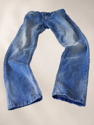 Blåa baggy jeans med slitningar lab - Säljer ett par blåa baggy jeans med slitningar på knäna och snyggt tvättad look. Jeansen har raka ben och klassisk femficksmodell. Perfekta för en avslappnad streetstil och tillverkade i bomullsdenim.
