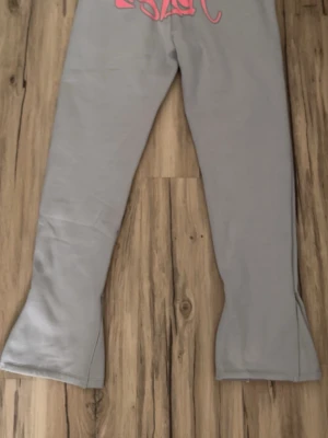 Syna world byxor tracksuit - Gråa syna world tracksuit byxor med rosa snören och mönster. Finns även hoodie som går att köpa tillsammans med byxorna om du vill, det blir lite billigare!