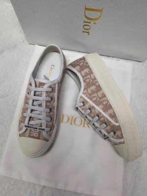 Dior Oblique sneakers  - Snygga Dior Oblique sneakers i beige och vitt med klassiskt monogrammönster. Skorna har vita snören, gummisula och detaljer i canvas. Märket syns tydligt på plösen och sidan. Perfekta för dig som vill ha en exklusiv touch till din outfit.