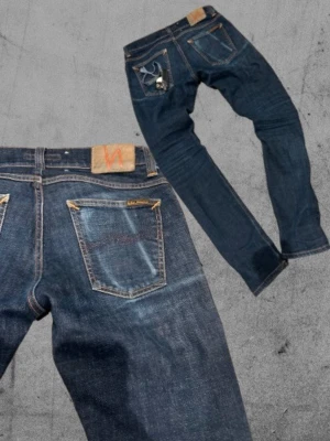 Nudie Jeans - Säljer ett par riktigt feta mörkblåa Nudie Jeans med mobil slitage på högra bakfickan. Riktigt snygga jeans som går till allt. Det är slim jim modellen så de sitter lite taijtare. De är 30/32 i storleken