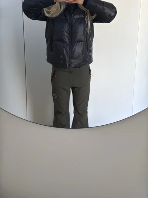 Gröna täckbyxor från DOPE - Säljer ett par gröna täckbyxor från DOPE  med raka ben och dragkedjor vid fickorna. Byxorna har en diskret logga på låret och är perfekta för skidåkning eller andra vinteraktiviteter. Snygg och sportig look med praktiska detaljer. Dessa byxor är lite mer (bagy) men har blivit för små för mig därav bilderna ni ser när jag har de i backen hur de är på.