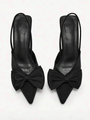 Svarta pumps med rosett - Stilrena svarta pumps med spetsig tå och dekorativ rosett framtill. Skorna har smala slingback-remmar och låg klack, vilket ger en elegant siluett. Helt oanvända.