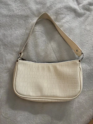 Krämvit axelväska - Stilren krämvit handväska med crocopräglat mönster och kort axelrem. Insidan är fodrad i matchande beige tyg. Perfekt för dig som gillar minimalistisk och trendig design.💗köpt för flera år sedan men bara använd några få gånger💗