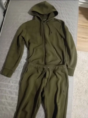 Ralph lauren - Mysig olivgrön loungewear-set från Polo Ralph Lauren med dragkedja på hoodien, fickor och justerbar huva. Matchande byxor med dragsko i midjan och sidofickor. Perfekt för chill dagar hemma.