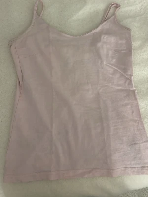 Ljusrosa linnetopp med smala band - Säljer en enkel och stilren ljusrosa linnetopp med smala axelband och v-ringad hals. Toppen är ärmlös och har en mjuk, bekväm passform som passar perfekt till sommaren. Perfekt att matcha med jeans eller kjol!
