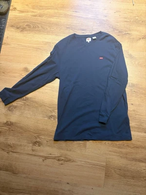 Mörkblå långärmad Levi's tröja - En stilren mörkblå långärmad tröja från Levi's med liten röd logotyp på bröstet. Tröjan har rund halsringning och är tillverkad i mjukt bomullstyg. 