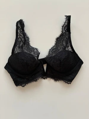 Vatterad bygel-BH i spets - Snygg svart bh i spets med djup v-ringning,  reglerbara axelband, och knäppning bak med hyskor och hakar. Den har vadderade kupor med bygel som formar bysten och ger bra stöd. Köp förra hösten men aldri använd. Från rökfritt hem men vi har hundar. 