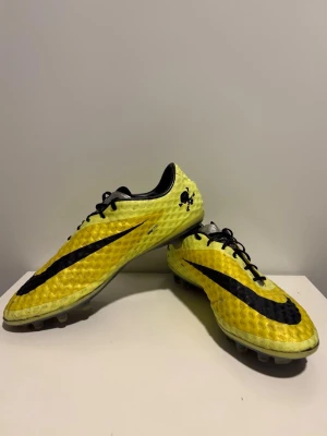 Nike Hypervenom gula fotbollsskor - Säljer ett par Nike Hypervenom fotbollsskor i gul och svart färg. Skorna har en texturerad ovandel för bättre bollkontroll, klassisk snörning och låg profil. Sulan har fasta dobbar för spel på gräsplan. Perfekta för dig som vill sticka ut på planen.