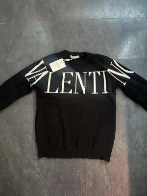 Valentino tröja - Snygg svart stickad tröja från Valentino med stor vit logotyp över bröstet och axlarna. Tröjan har rund halsringning och långa ärmar. Perfekt för dig som gillar exklusiva märken och vill sticka ut med en trendig look.
