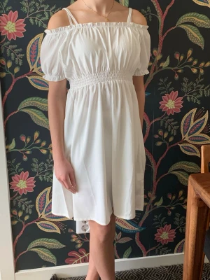Vit offshoulder kortklänning - Söt vit kort klänning med offshoulder och puffärmar. Nyskick, endast använd en gång. Perfekt till skolavslutning. Storlek 152.