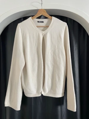 Vit kofta från Gina Tricot - Stilren vit kofta från Gina Tricot med rund halsringning och en knapp upptill. Koftan har långa ärmar och ribbade muddar vid ärmslut och nederkant. Perfekt att slänga över en topp för en enkel och clean look.