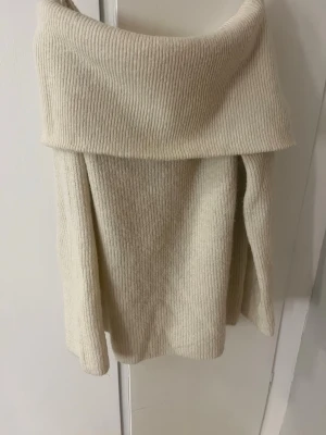  off shoulder stickad tröja - Säljer en krämvit stickad tröja med bred off shoulder-krage. Tröjan har långa ärmar och är ribbstickad för en mysig och trendig look. Perfekt för dig som gillar en avslappnad men ändå snygg stil. Materialet känns mjukt och skönt mot huden.