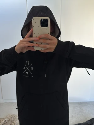 Svart vindjacka med huva från Dope snow - Snygg svart vindjacka från Dope snow med stor huva och magficka. Jackan har ett vitt tryck på bröstet och ribbade muddar vid ärmsluten. Perfekt för blåsiga dagar och enkel att matcha med olika outfits. Detta är en liten tunnare variant vilket kan vara skönt också🤗🤗