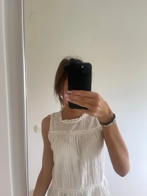 Vit ärmlös blus från ZARA - Säljer en söt vit ärmlös blus från ZARA med broderade detaljer upptill och volangkant vid halsen. Blusen har en luftig och lätt struktur, perfekt för varma dagar. Knappt använd, pris går att diskutera 💕