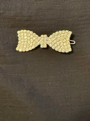 Silverfärgad hårklämma i rosettform - Snygg hårklämma i form av en rosett, helt täckt med små silverfärgade detaljer som ger ett glittrigt intryck. Klämman är gjord i metall och har ett klassiskt spänne på baksidan som håller håret på plats. Perfekt accessoar för att lyfta din frisyr. 