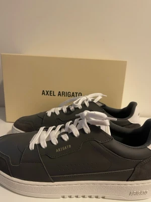 Axel Arigato Clean90 gråa sneakers med vit sula - Oanvända stilrena svarta sneakers från Axel Arigato med vit sula och vita skosnören. Skorna har detaljer i läder samt vit hälkappa med logga. Perfekta för en trendig och clean look.