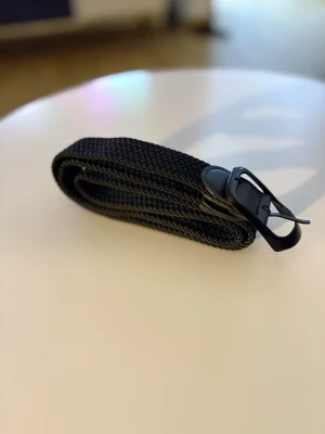 Svart flätat bälte med metallspänne - Snyggt svart flätat bälte med ett stilrent metallspänne. Bältet har en enkel och clean design som passar till de flesta outfits. Perfekt accessoar för att lyfta din look. Svart flätat stretchbälte med svart metallspänne. Den sitter bekvämt och kan justeras enkelt utan fasta hål.