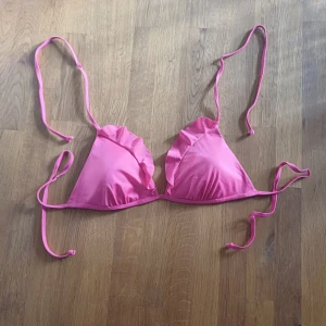 Rosa bikiniöverdel med volang - Söt rosa bikiniöverdel med volangdetaljer på kuporna och smala knytband i nacken och ryggen. Perfekt för lata dagar på stranden eller poolen. Enkel trekantsmodell som ger en ungdomlig och trendig look.