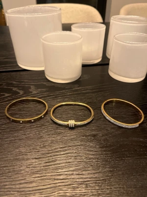 Guldigt armband med pärldetaljer - 3X bundle Snygga armband i guldfärgad metall med infällda små pärlor runt om. Stilren och modern design som passar perfekt till din vardagsstil. Armbandet har en slät, blank yta och rund form. Alla 3 för 299!