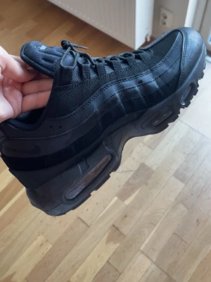 Nike Air Max 95 Triple Black sneakers - Snygga Nike Air Max 95 i helsvart färg. Skorna har en chunky sula med synliga Air-enheter, ovandel i mesh och läder samt klassiska vågiga paneler. Perfekta för dig som gillar streetwear och vill ha en ikonisk sneaker med grym komfort.
