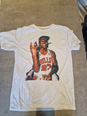 Vit t-shirt med Bulls-tryck från Boutik - Vit t-shirt från Boutik med ett stort färgglatt tryck av en basketspelare i Bulls-tröja på framsidan. Klassisk rund halsringning och korta ärmar. Perfekt för dig som gillar sportiga och unika prints.