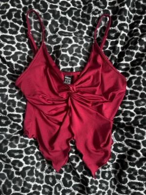 Vinröd linnetopp - Trendig vinröd linnetopp från SHEIN med smala axelband och snygg knutdetalj framtill. Toppen har en spetsig nederkant och är gjord i ett glansigt polyestertyg som känns mjukt mot huden. Perfekt för att lyfta vilken outfit som helst. Oanvänd. 