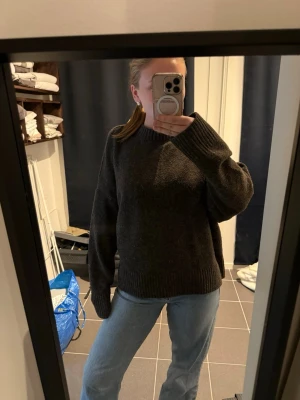 Mörkbrun stickad tröja Vero Moda - Mysig mörkgrå stickad tröja från Vero Moda med avslappnad passform och bred ribbad mudd vid hals, ärmslut och nederkant. Tillverkad i mjukt material som känns skönt mot huden. Perfekt för kyliga dagar.