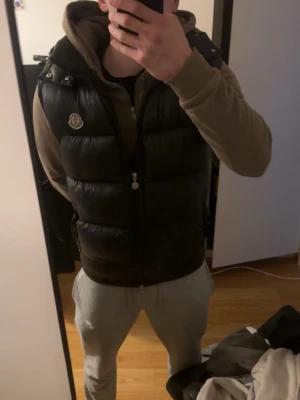 Svart dunväst från Moncler - Snygg svart dunväst från Moncler med hög krage och avtagbar huva. Västen har dragkedja framtill, två fickor med dragkedja och Moncler-logga på bröstet. Priset därav jag är inte har nått bevis på att den är äkta, men jag köpte av min kompis för ungefär 2 år sedan och han sa att den va äkta. Nfc och qr kod funkar däremot!