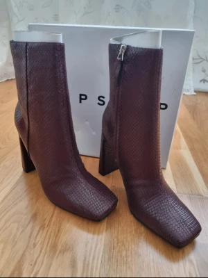 Bruna stövletter med ormskinnsmönster - Snygga bruna stövletter från Topshop med trendigt ormskinnsmönster och fyrkantig tå. Skorna har en hög blockklack och dragkedja på sidan för enkel på- och avtagning. Perfekta för att lyfta din outfit med en cool och modern touch.