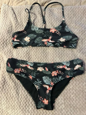 Svart bikini med blommigt mönster - Snygg svart bikini med tropiskt mönster. Överdelen har smala axelband och sportig form, medan underdelen har klassisk passform. Perfekt för stranden eller poolen! Pris kan diskuteras! 