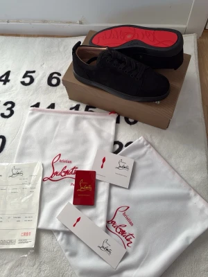 Svarta Christian Louboutin goyard plånbok medkommer vid köp - Säljer ett par svarta sneakers från Christian Louboutin med klassisk röd sula. Skorna är i mocka och har svarta skosnören samt diskreta sömmar. Kommer med originalkartong, dustbags och äkthetskort. Perfekta för dig som gillar exklusiva detaljer och streetstyle.