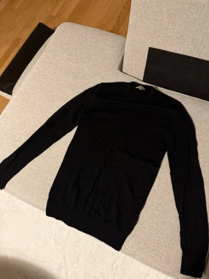 Svart stickad tröja H&M - Snygg svart stickad tröja från H&M i slim fit-modell. Tröjan har rund halsringning, långa ärmar och ribbade muddar vid ärmslut och nederkant. Perfekt basplagg för lager på lager och enkel att matcha med olika stilar.
